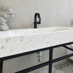 A marble sink with black faucet and white walls.